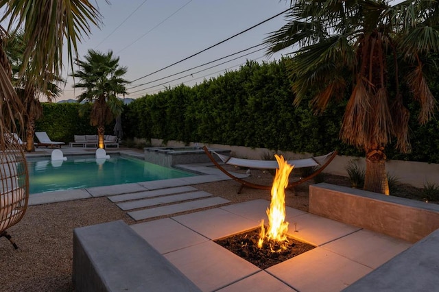 pool at dusk featuring a patio area, an in ground hot tub, and an outdoor fire pit