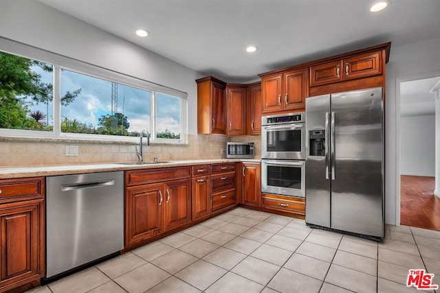 kitchen featuring tasteful backsplash, sink, light tile patterned floors, and appliances with stainless steel finishes