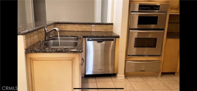 kitchen with stainless steel appliances, sink, light tile patterned floors, and dark stone counters