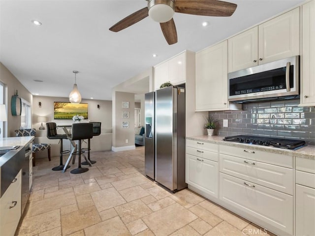 kitchen with pendant lighting, appliances with stainless steel finishes, white cabinetry, light stone countertops, and decorative backsplash