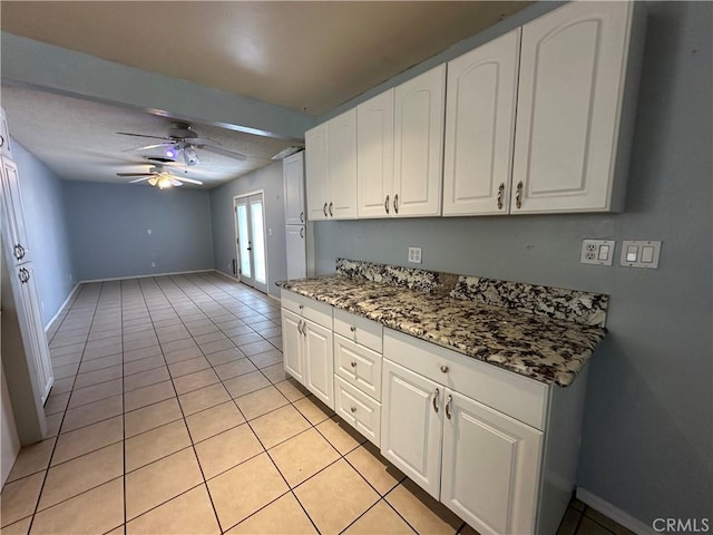 kitchen featuring white cabinetry, ceiling fan, dark stone counters, and light tile patterned flooring