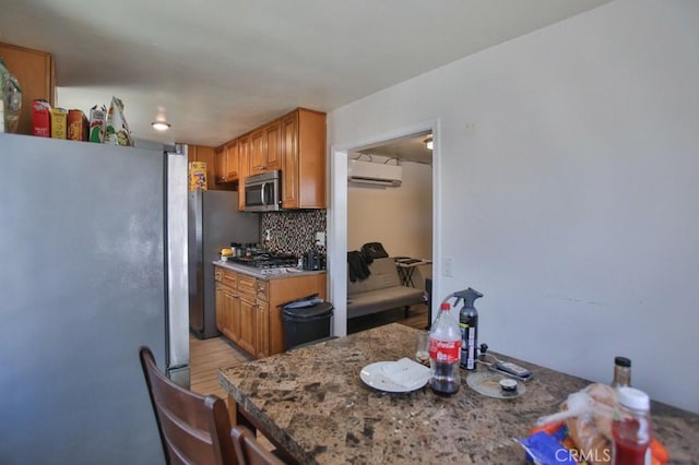 kitchen featuring a wall unit AC, light wood-style floors, appliances with stainless steel finishes, brown cabinets, and tasteful backsplash