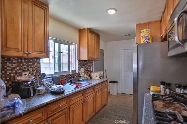 kitchen featuring stainless steel appliances, backsplash, brown cabinetry, a sink, and wood finished floors