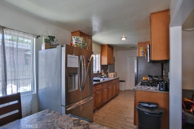 kitchen with stainless steel appliances, light wood-type flooring, brown cabinetry, and tasteful backsplash