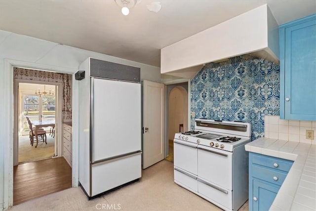 kitchen with paneled refrigerator, tile countertops, blue cabinetry, and range with two ovens