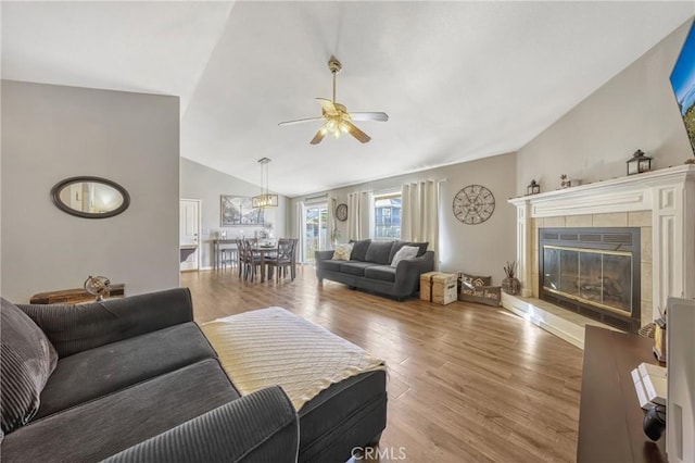 living room featuring hardwood / wood-style flooring, vaulted ceiling, ceiling fan, and a tile fireplace