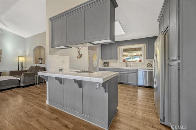 kitchen featuring a breakfast bar, dishwasher, gray cabinetry, tile counters, and kitchen peninsula