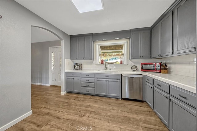 kitchen with sink, dishwasher, gray cabinetry, backsplash, and light wood-type flooring