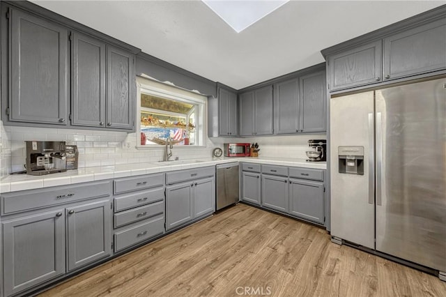 kitchen featuring sink, gray cabinets, stainless steel appliances, tile countertops, and light wood-type flooring