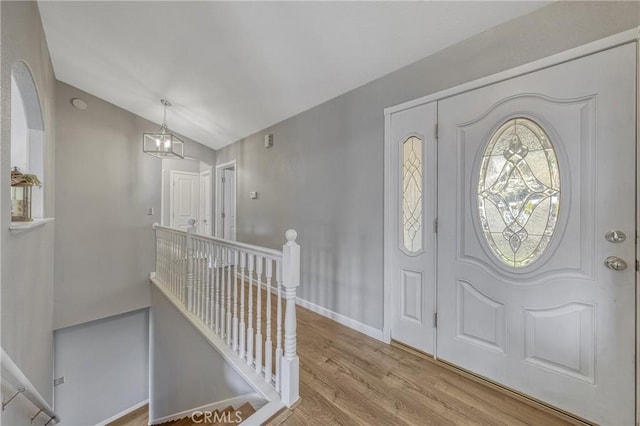 foyer entrance with an inviting chandelier, vaulted ceiling, and light wood-type flooring