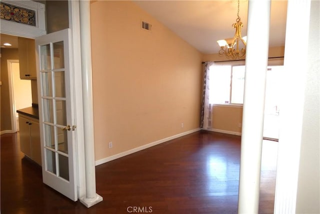 empty room featuring visible vents, baseboards, lofted ceiling, an inviting chandelier, and dark wood-style flooring