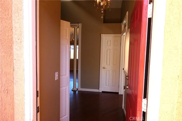 hall with baseboards, dark wood-type flooring, and a chandelier