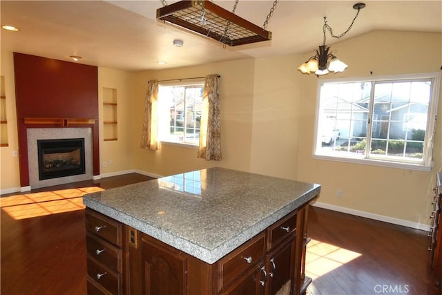 kitchen with built in shelves, dark wood-type flooring, baseboards, a tiled fireplace, and vaulted ceiling