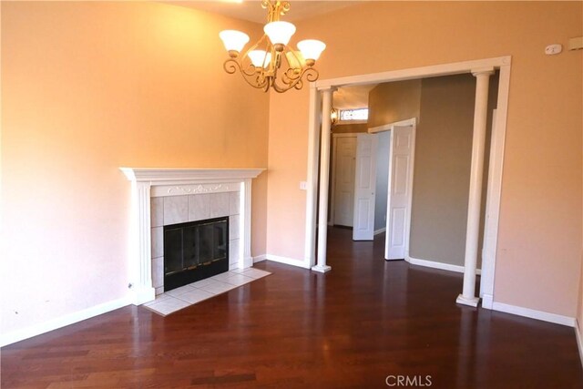 unfurnished living room with ornate columns, a tile fireplace, dark wood-type flooring, and a notable chandelier