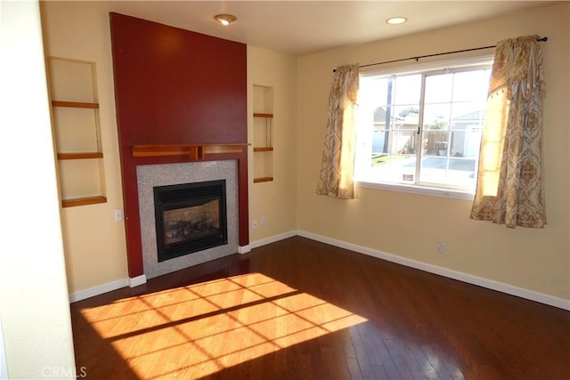 unfurnished living room featuring built in features, baseboards, wood finished floors, and a fireplace