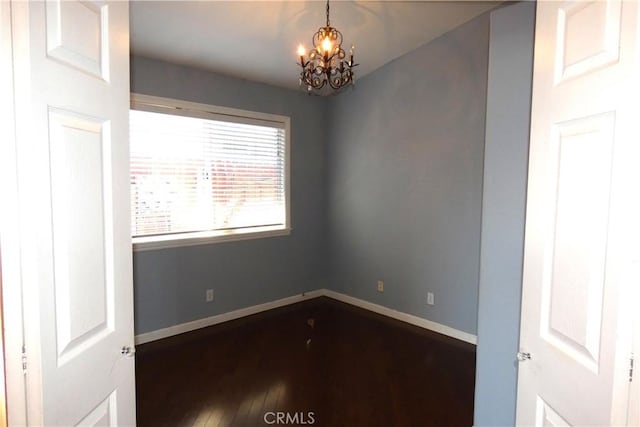 empty room with an inviting chandelier, dark wood-type flooring, and baseboards