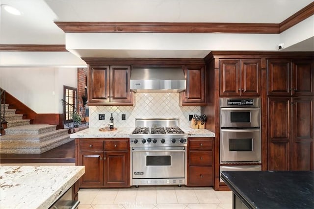 kitchen featuring appliances with stainless steel finishes, backsplash, light tile patterned floors, light stone countertops, and wall chimney exhaust hood