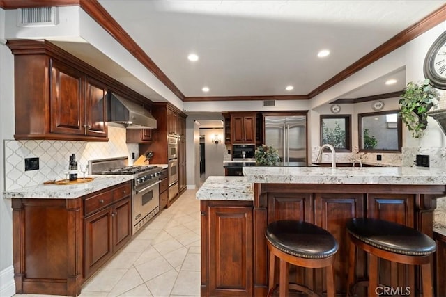 kitchen with ornamental molding, a breakfast bar, wall chimney range hood, and premium appliances