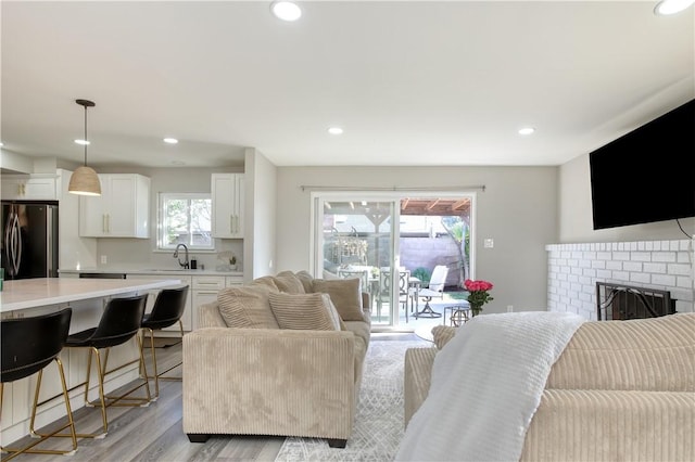 living room with a brick fireplace, sink, and light hardwood / wood-style floors