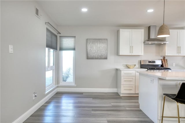 kitchen with white cabinetry, a breakfast bar area, hanging light fixtures, wall chimney range hood, and stainless steel range oven