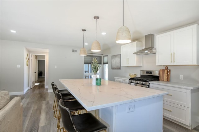 kitchen with white cabinetry, wall chimney exhaust hood, stainless steel range with gas stovetop, and a kitchen island