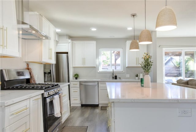 kitchen with sink, stainless steel appliances, white cabinets, decorative light fixtures, and wall chimney exhaust hood