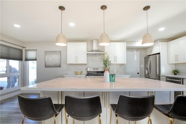 kitchen featuring wall chimney exhaust hood, white cabinetry, hanging light fixtures, stainless steel appliances, and a large island