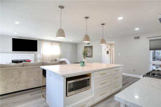 kitchen featuring a center island, stainless steel microwave, light stone countertops, white cabinets, and decorative light fixtures