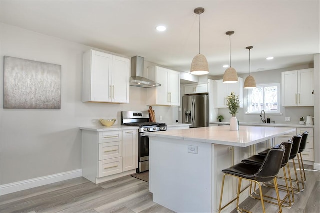 kitchen with a kitchen island, appliances with stainless steel finishes, white cabinetry, hanging light fixtures, and wall chimney range hood