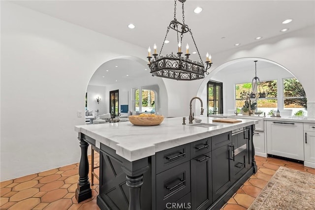 kitchen featuring sink, pendant lighting, light stone countertops, a kitchen island with sink, and white cabinets