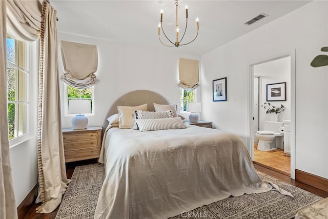 bedroom with multiple windows, dark hardwood / wood-style floors, connected bathroom, and an inviting chandelier