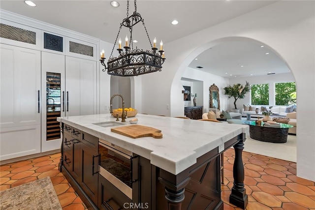 kitchen featuring light tile patterned flooring, sink, a center island with sink, pendant lighting, and light stone countertops