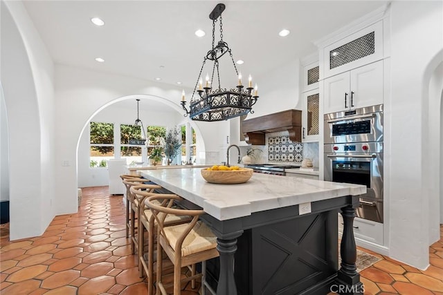 kitchen with white cabinetry, a center island, tasteful backsplash, light stone countertops, and stainless steel double oven