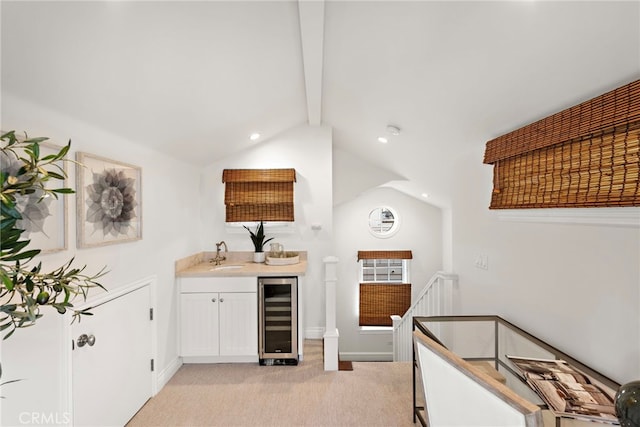 kitchen with sink, lofted ceiling with beams, light colored carpet, beverage cooler, and white cabinets