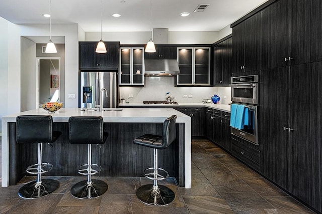 kitchen featuring a breakfast bar, extractor fan, decorative light fixtures, a center island with sink, and stainless steel appliances