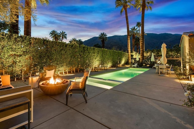 patio terrace at dusk with a fenced in pool, a mountain view, and a fire pit