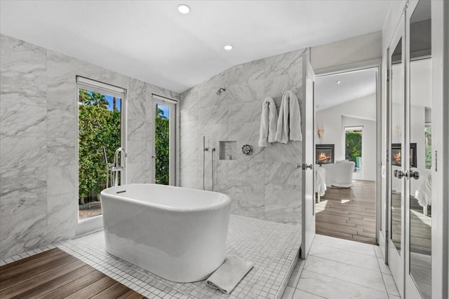 bathroom with vaulted ceiling, shower with separate bathtub, a fireplace, tile walls, and tile patterned floors