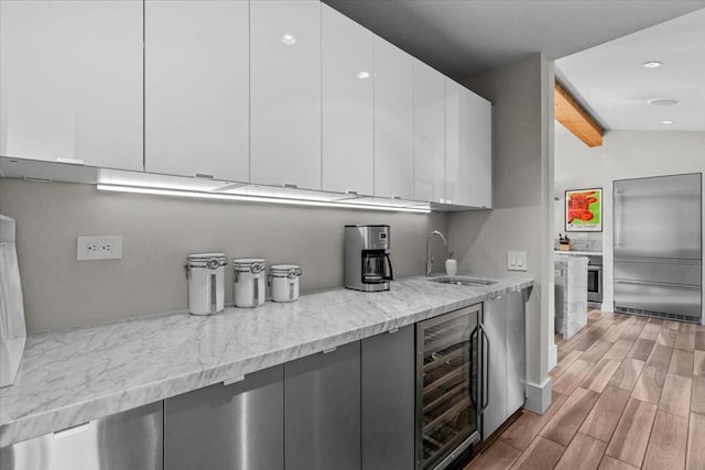 kitchen featuring white cabinetry, sink, beverage cooler, and light stone counters