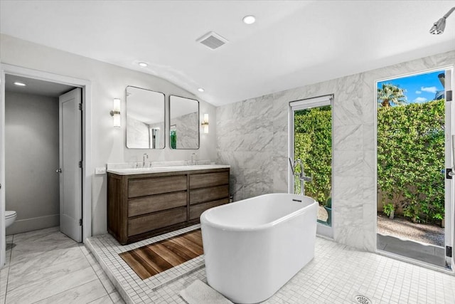 bathroom featuring tile walls, vanity, a bath, vaulted ceiling, and toilet