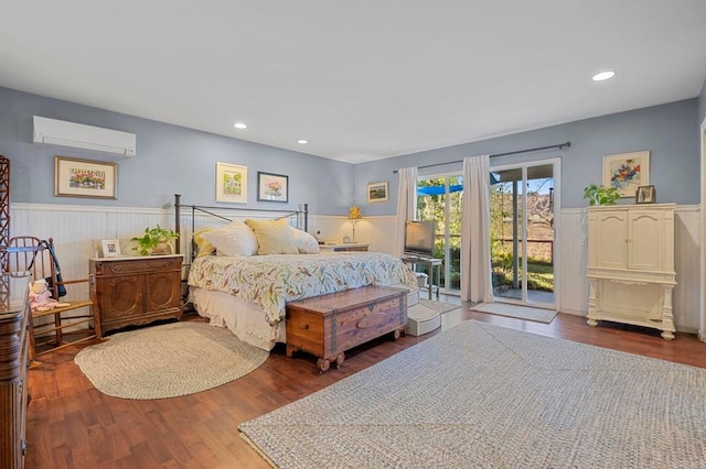 bedroom with wood finished floors, wainscoting, and a wall mounted AC