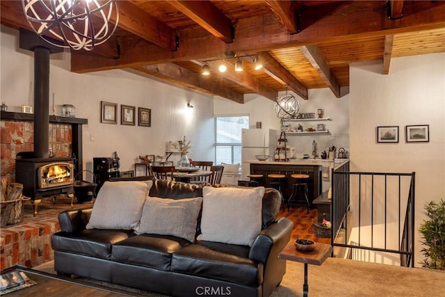 living room featuring hardwood / wood-style flooring, beam ceiling, track lighting, a chandelier, and a wood stove