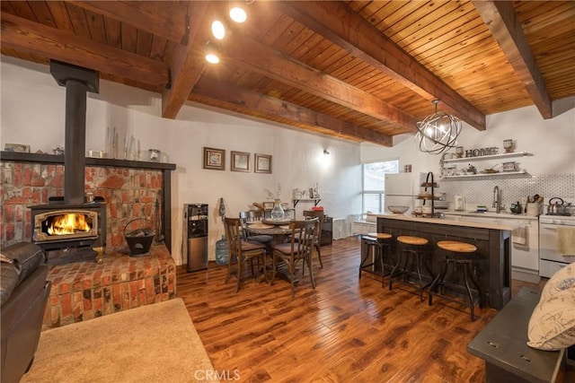 dining room with beamed ceiling, dark wood-type flooring, a wood stove, and wooden ceiling