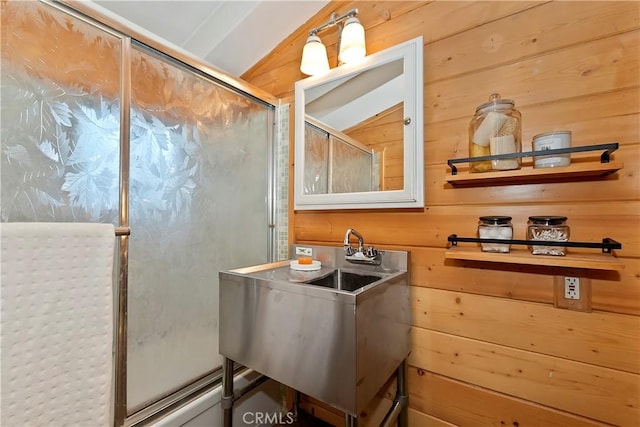 bathroom featuring sink, wooden walls, a shower with shower door, and vaulted ceiling