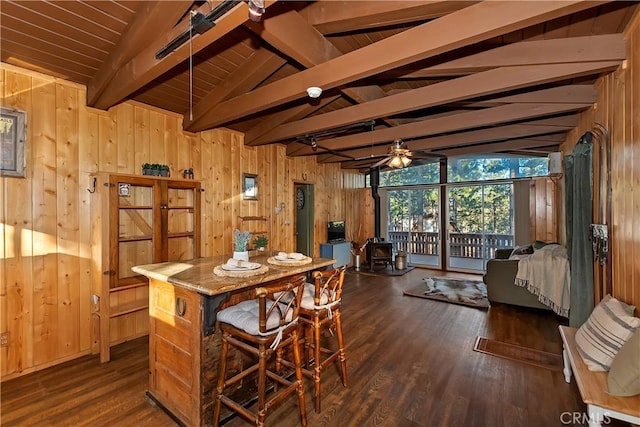 dining room with a wood stove, ceiling fan, lofted ceiling with beams, dark hardwood / wood-style flooring, and wood walls