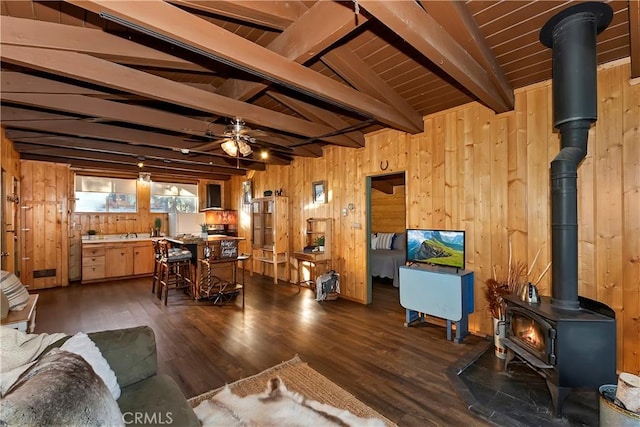 living room with wooden walls, lofted ceiling with beams, a wood stove, wood ceiling, and ceiling fan