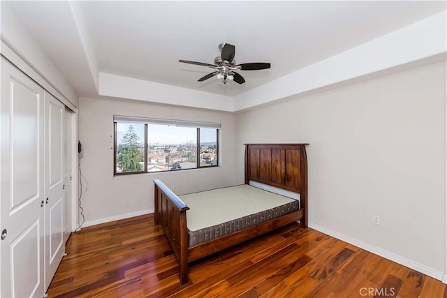 bedroom featuring dark wood-type flooring, ceiling fan, a raised ceiling, and a closet