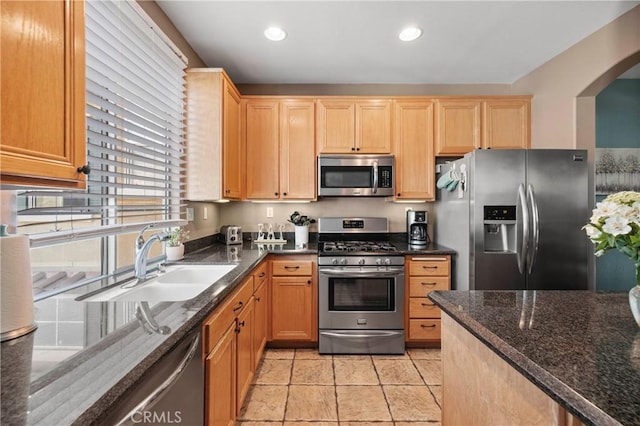 kitchen with dark stone countertops, sink, light tile patterned floors, and appliances with stainless steel finishes