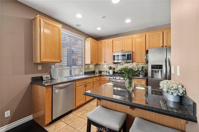 kitchen featuring sink, a breakfast bar area, stainless steel appliances, dark stone counters, and light brown cabinets