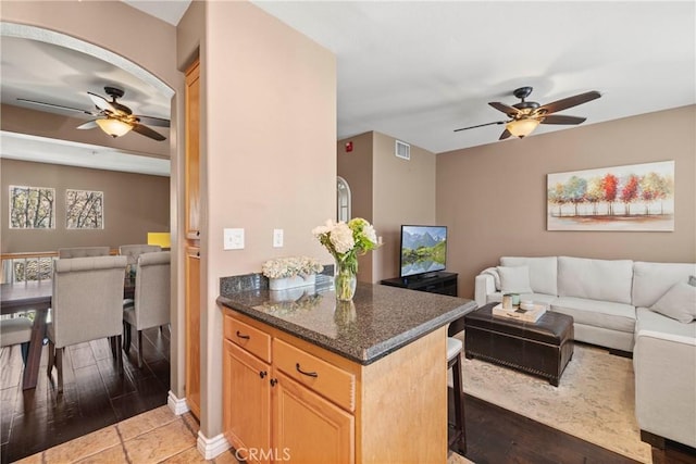 kitchen featuring ceiling fan, dark stone countertops, hardwood / wood-style floors, a kitchen bar, and light brown cabinets