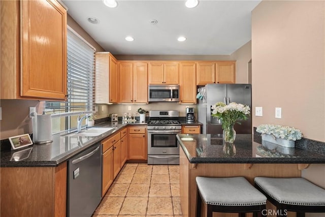 kitchen featuring sink, a kitchen bar, stainless steel appliances, light tile patterned flooring, and dark stone counters